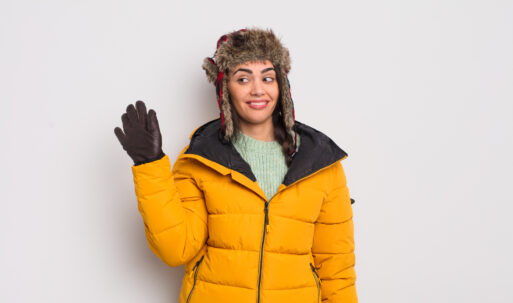 pretty hispanic woman smiling happily, waving hand, welcoming and greeting you. cold weather concept
пуховик