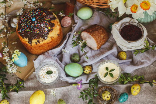 Traditional Easter food. Homemade easter bread, natural dyed easter eggs, ham, beets, butter, cheese on linen napkin on rustic table with spring flowers. Top view.
пасха, антипасха, фомино воскресенье