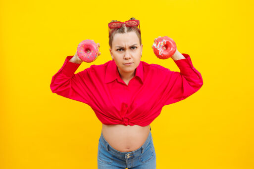 Smiling pregnant woman with sweet cakes in her hands on a yellow background. Delicious sweet donuts in the hands of a woman. Harmful food
похудения, жир